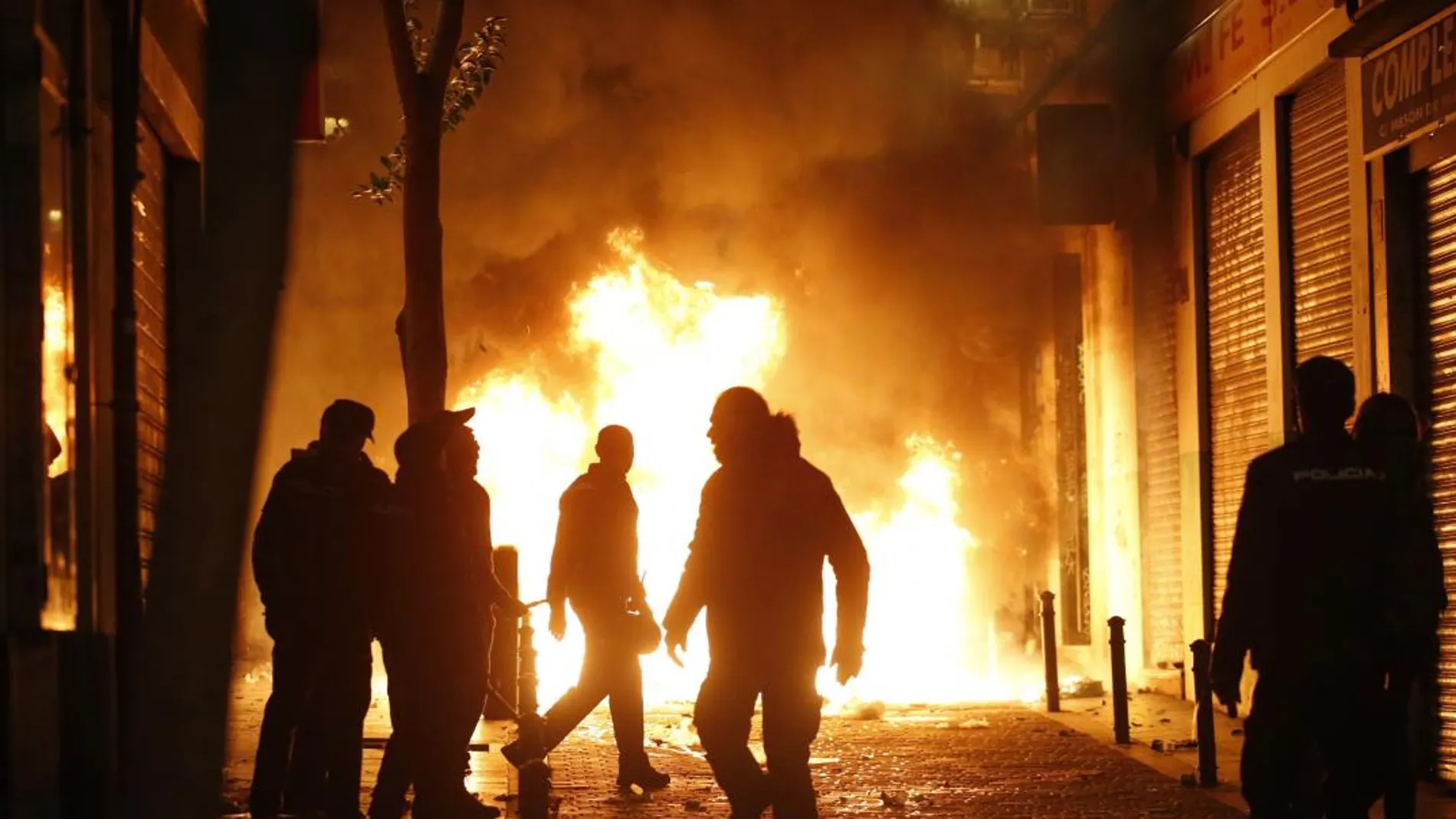 Contenedores incendiados en la calle Mesón de Paredes con la calle del Oso, en el barrio de Lavapiés de Madrid, tras la muerte de un mantero de un paro cardíaco. EFE/JAVIER LIZÓN
