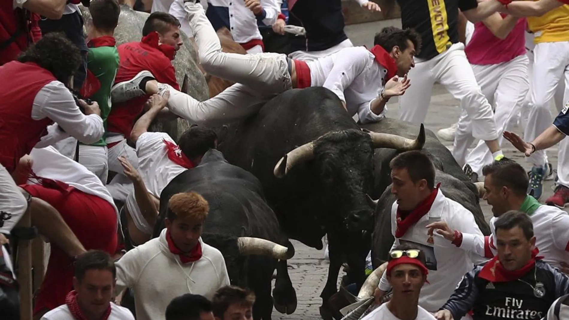 Dos astados de la ganadería de Miura, de Lora del Río (Sevilla), voltean a un mozo en el tramo final que precede al callejón de entrada a la Plaza de Toros durante el octavo y último encierro de los Sanfermines