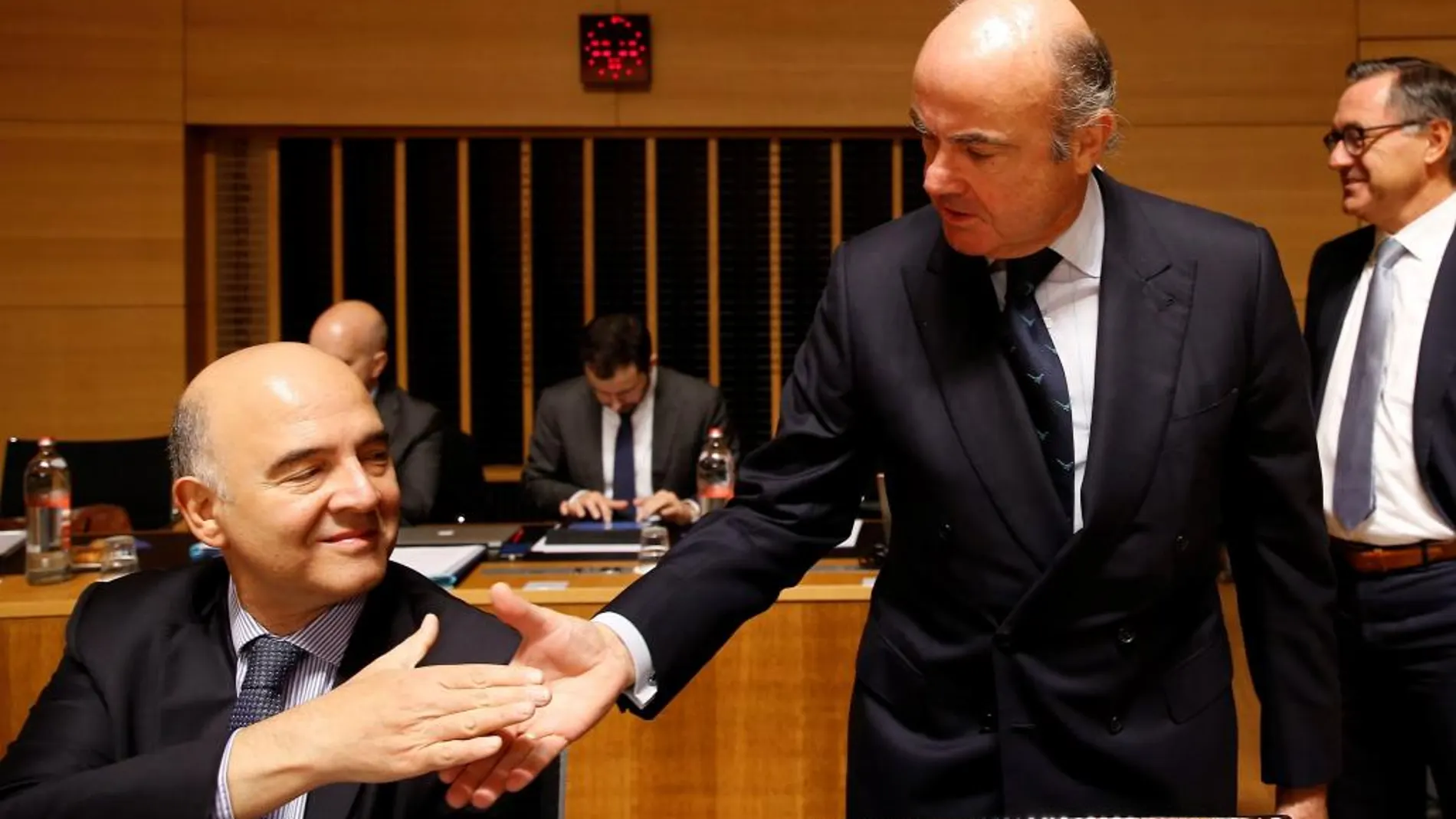 El ministro de Economía español, Luis de Guindos (dcha), saluda al comisario europeo de Asuntos Económicos y Financieros, Pierre Moscovici,