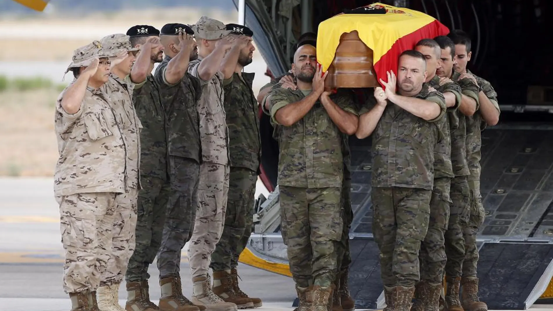 El féretro envuelto con la bandera nacional, es trasladado a hombros hasta el coche fúnebre a su llegada a la terminal militar del aeropuerto de Manises