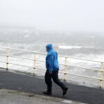 Un hombre camina junto al fuerte oleaje en la costa del Condado de Clare