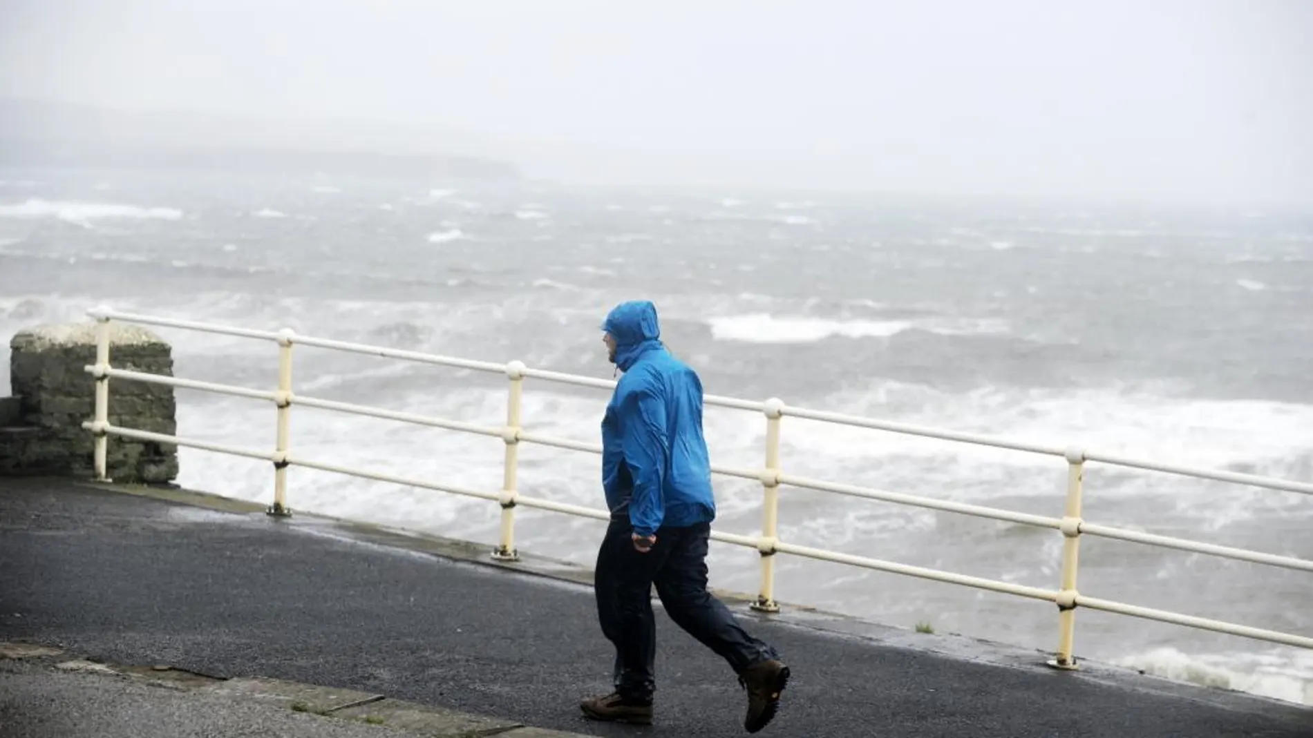 Un hombre camina junto al fuerte oleaje en la costa del Condado de Clare