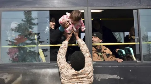 Una mujer da su bebé a un militar a su llegada a un campo de refugiados
