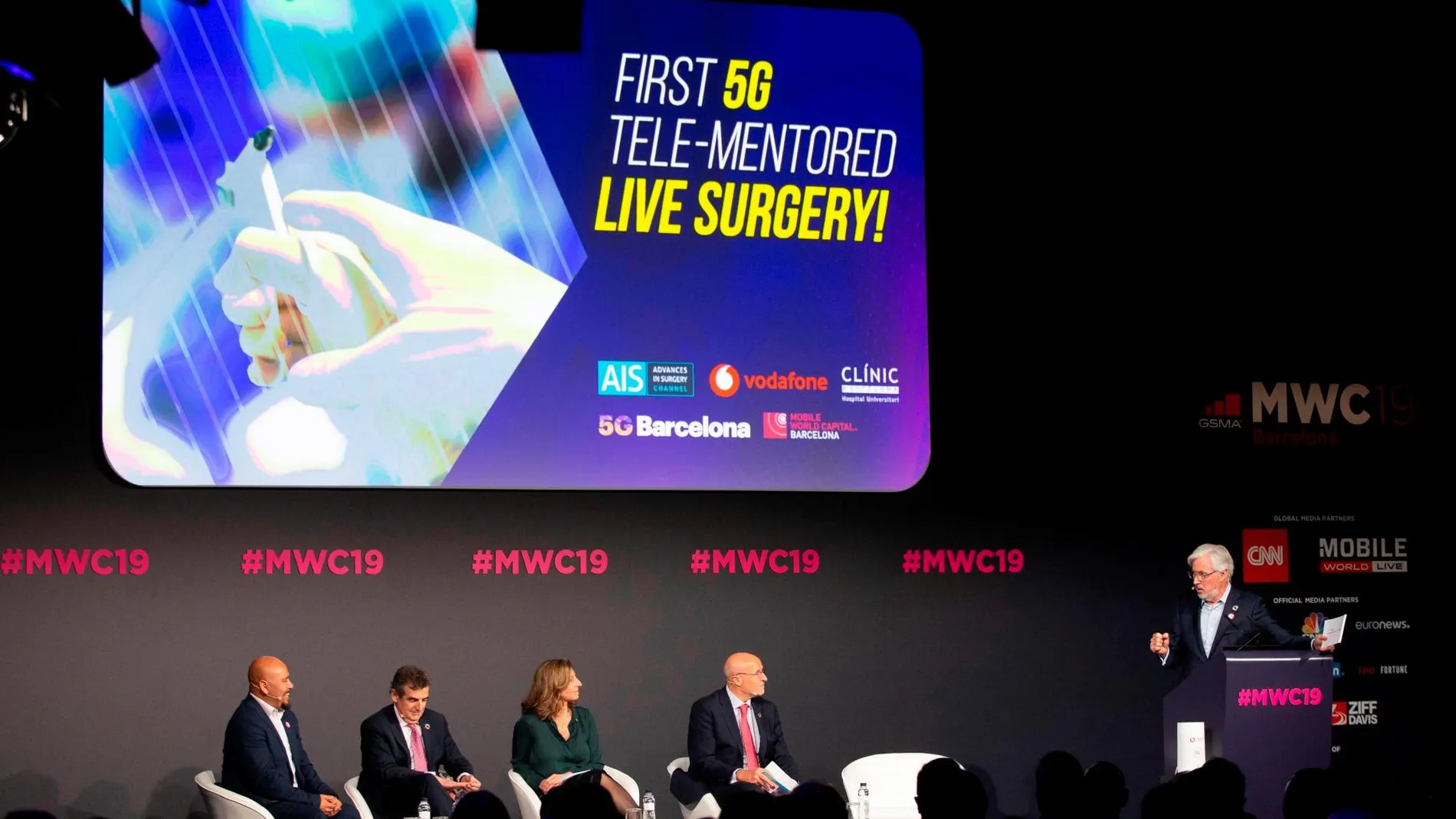 El jefe de la unidad de cirugía gastrointestinal del Hospital Clínic de Barcelona, Antonio de Lacy (d), monitora y dirige a su equipo desde el auditorio del MWC, durante una cirugía de extracción de un tumor en el colon de un paciente a través de una tableta conectada por tecnología 5G con un nuevo quirófano construido en el Hospital Clínic de Barcelona. EFE/Enric Fontcuberta