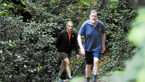 El ex presidente del Gobierno, Mariano Rajoy, con uno de sus acompañantes habituales a la hora de hacer ejercicio, José Benito Suárez, en su paseo mañanero en la ruta Da Pedra e Da Agua en el río Armenteira, el día de las primarias del PP
