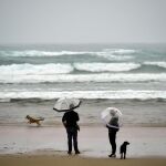 Dos personas, caminan por la playa de Zurriola en un día lluvioso