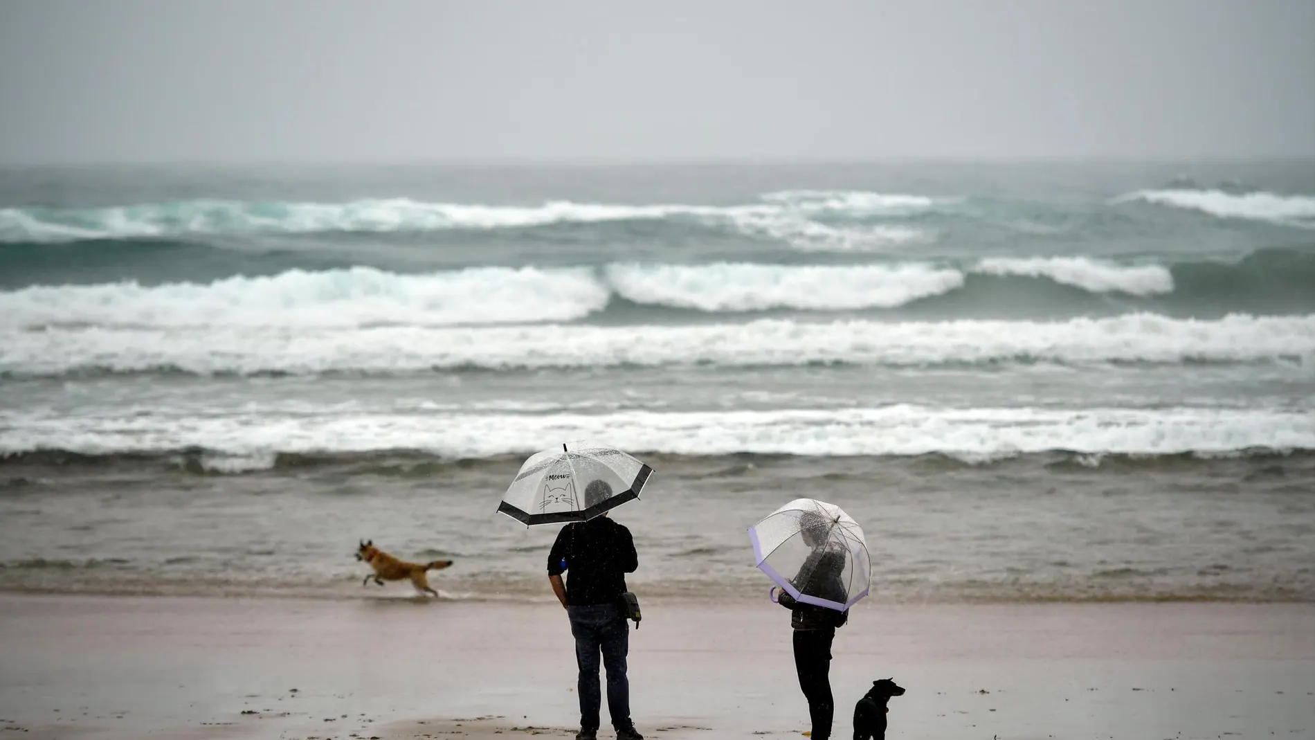 Dos personas, caminan por la playa de Zurriola en un día lluvioso