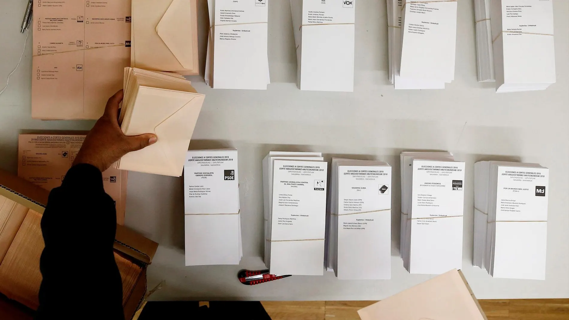 Una persona coloca en la mesa de un colegio electoral de Pamplona las papeletas con las diferentes opciones políticas