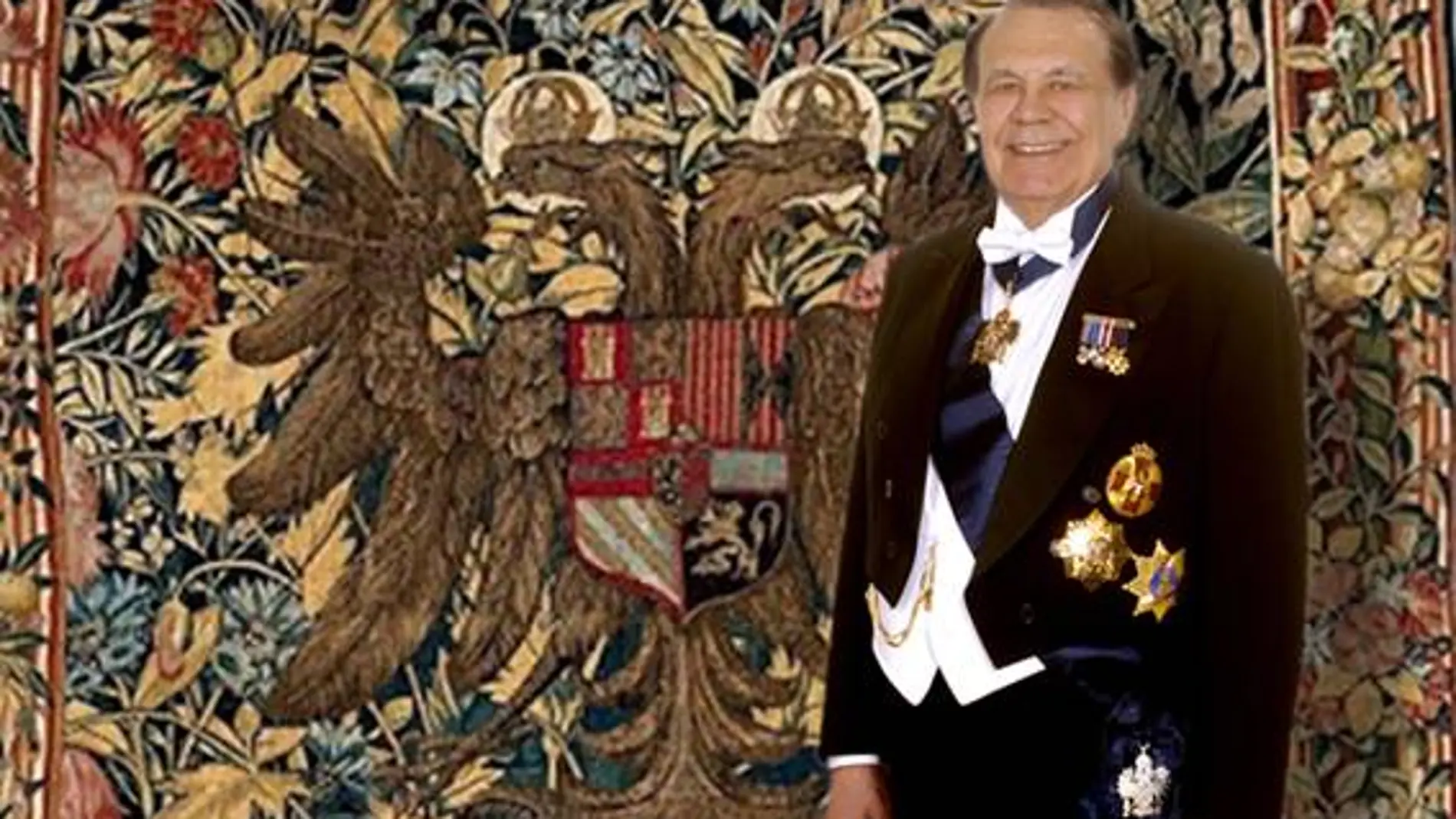 El escritor Manuel Muñoz Hidalgo, tras la Investidura, posando junto al tapiz que contiene el escudo de Carlos V