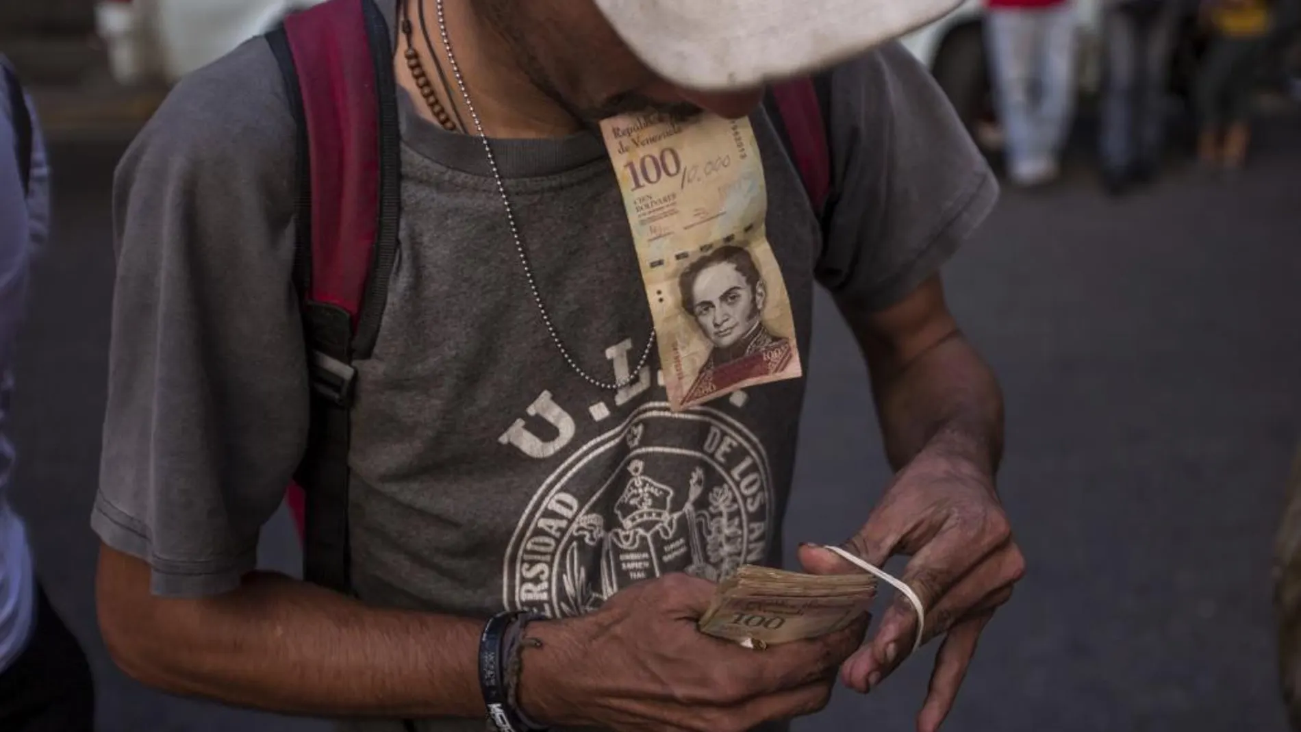 Un hombre organiza sus billetes de 100 bolívares mientras hace fila en las inmediaciones del Banco Central de Venezuela
