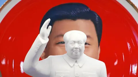 Una escultura de Mao Zedong enfrente de un souvenir con la imagen del actual presidente chino, Xi Jinping, desplegados en una tienda junto a la plaza de Tiananmen, en Pekín