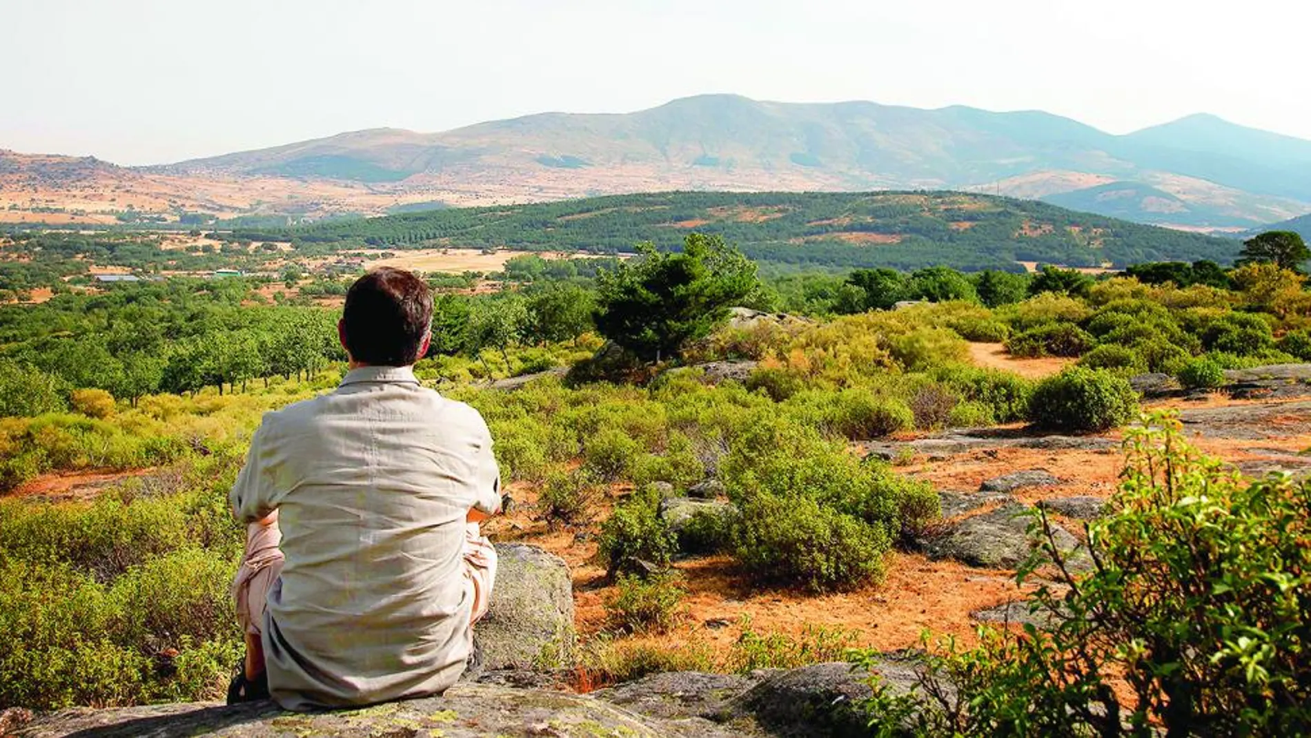 Un hombre observa, sentado, unas de las vistas que ofrece a los visitantes la sierra de Guadarrama desde Segovia.