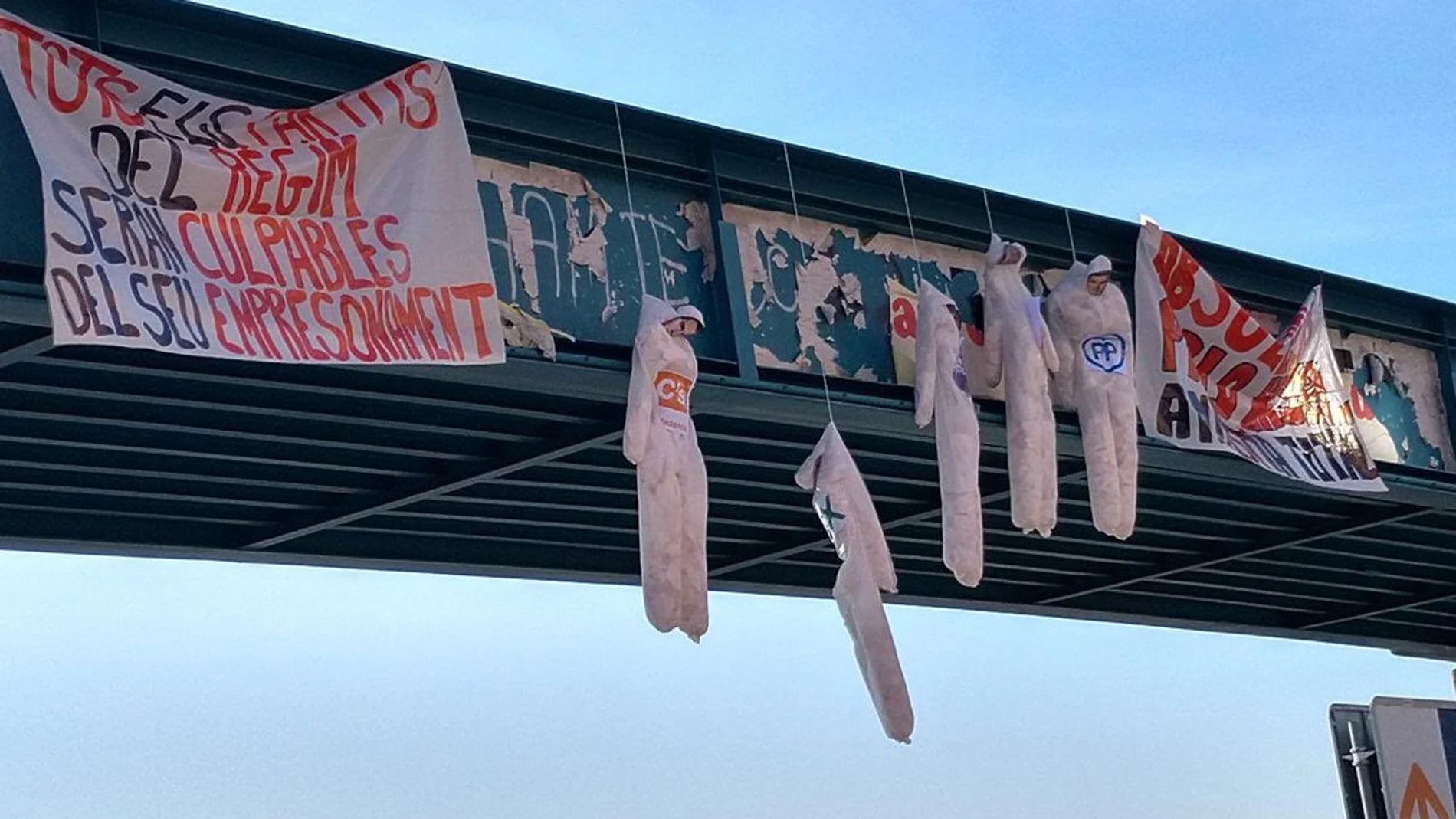 Las dos pancartas y los cinco muñecos colgados en un puente de Lérida
