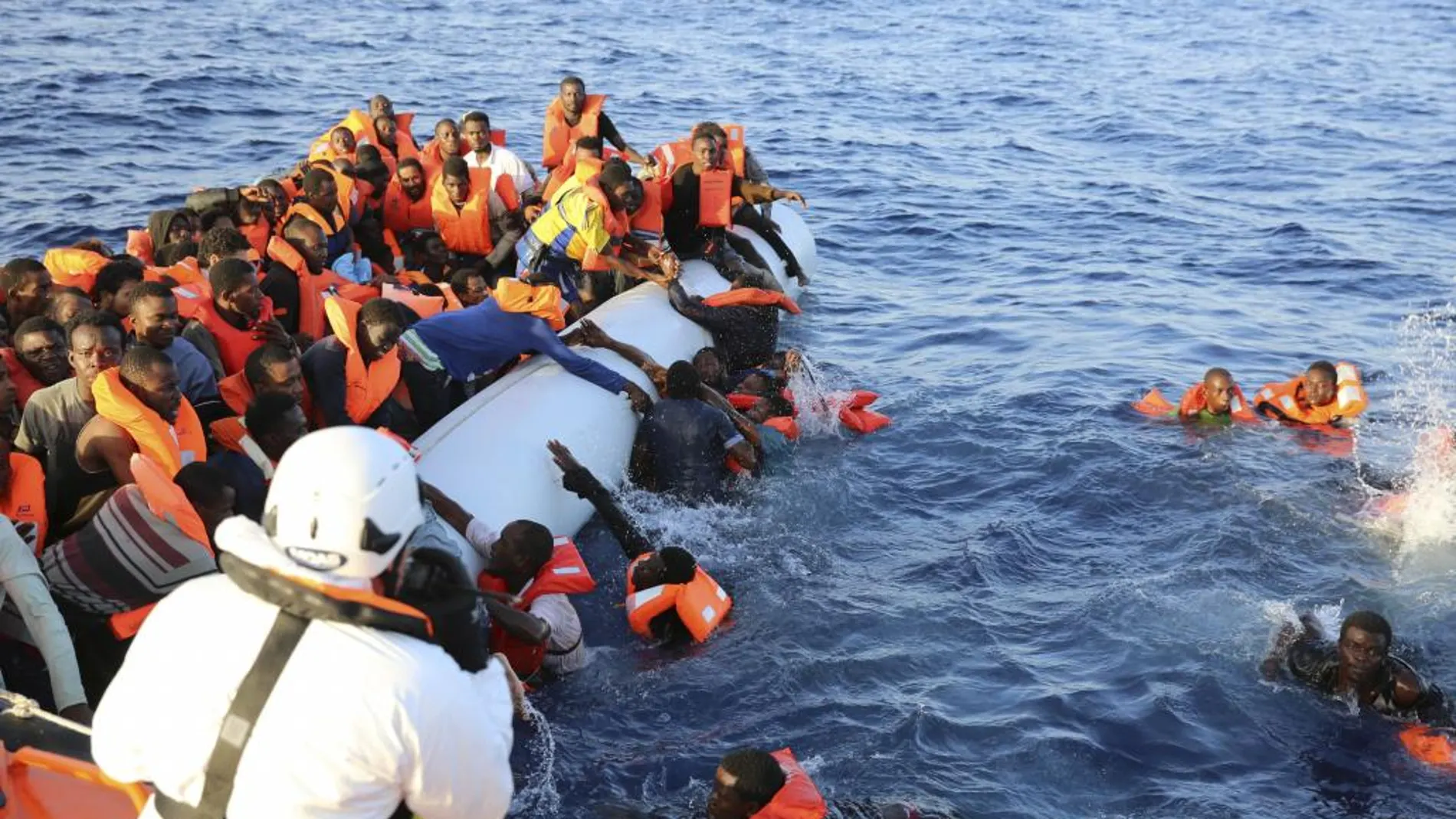 Varios inmigrantes, que han caído al agua, son rescatados por sus compañeros y por miembros de Cruz Roja cerca de Malta