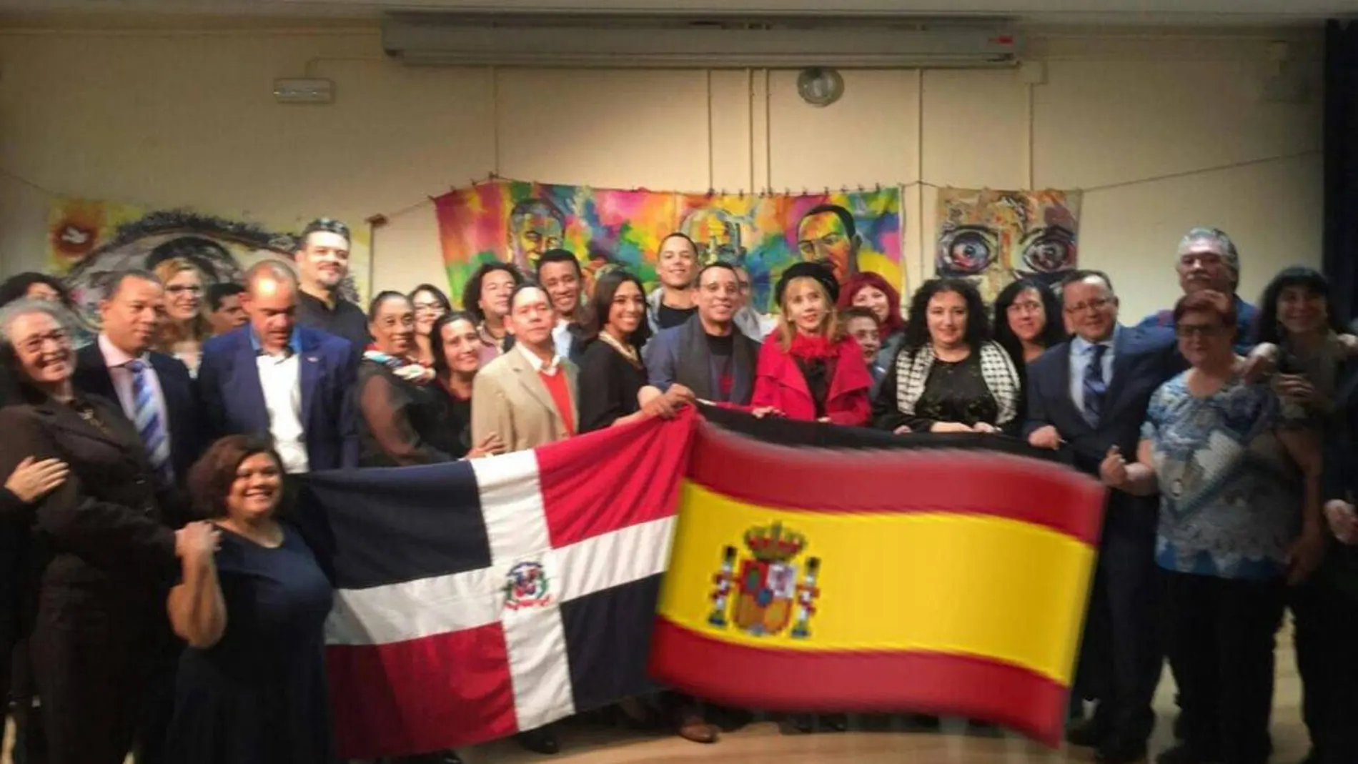 Genaro Roble (Yiyoh) y Sarah Merán, autores del proyecto «Lienzos Sueltos por La Paz» posando en una foto de familia, mostrando las banderas de R. Dominicana y de España