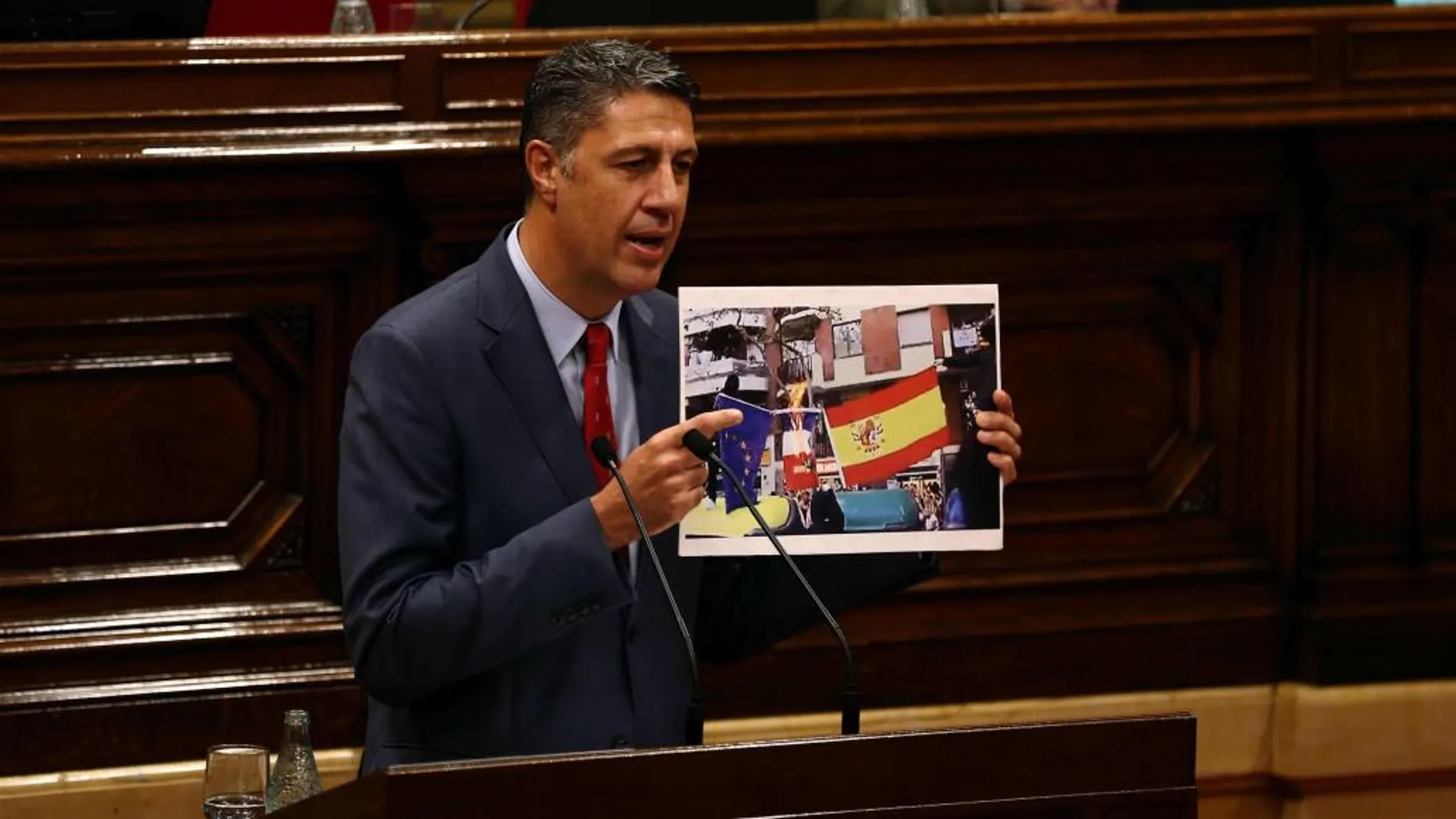 El líder del PPC, Xavier García Albiol, muestra una fotografía de banderas quemadas durante su intervención en la segunda jornada del pleno de la cuestión de confianza planteada por el presidente de la Generalitat, Carles Puigdemont