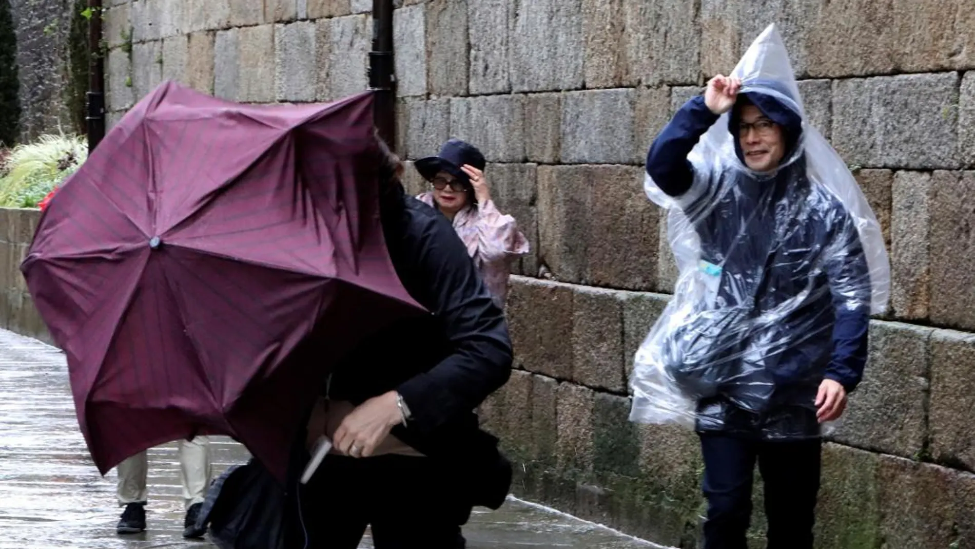 Turistas japoneses luchan por no perder sus paraguas esta mañana en la Plaza del Obradoiro de Santiago de Compostela