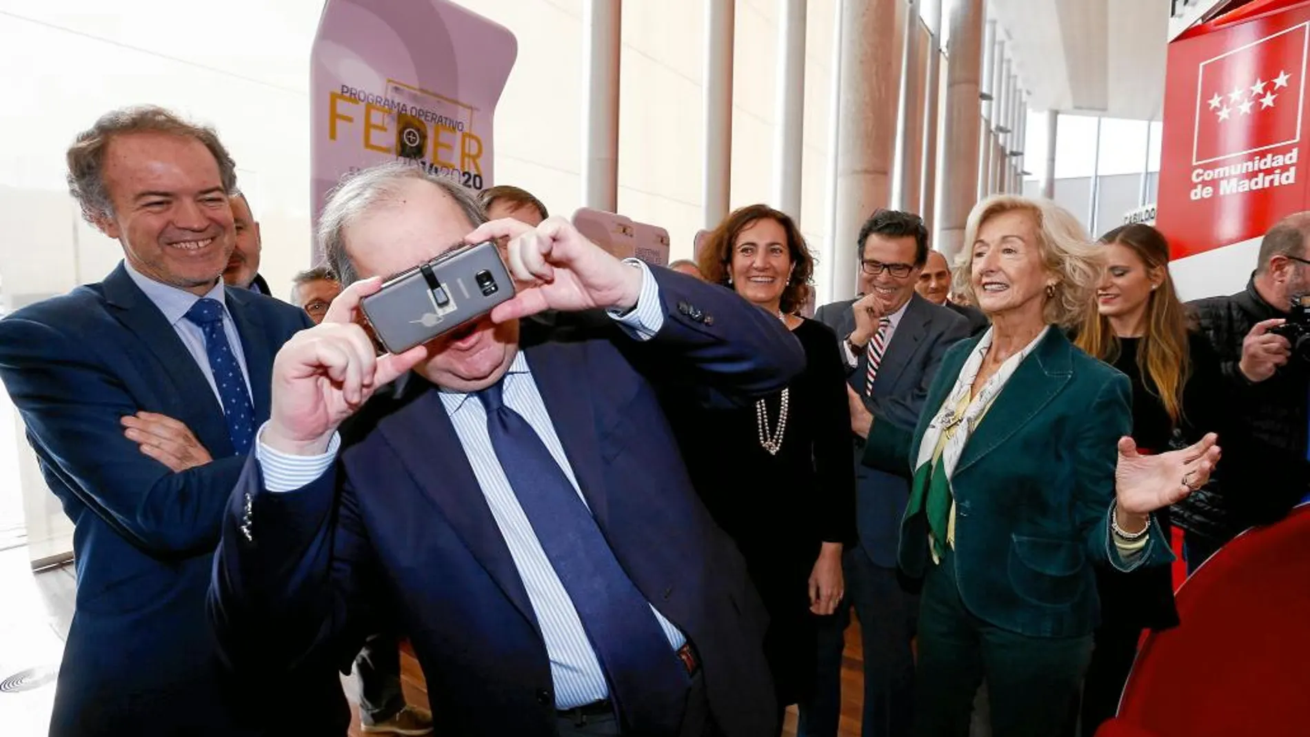 El presidente de la Junta prueba unas gafas adaptadas a modo visor a un móvil en el pabellón de Madrid de AR&amp;PA.