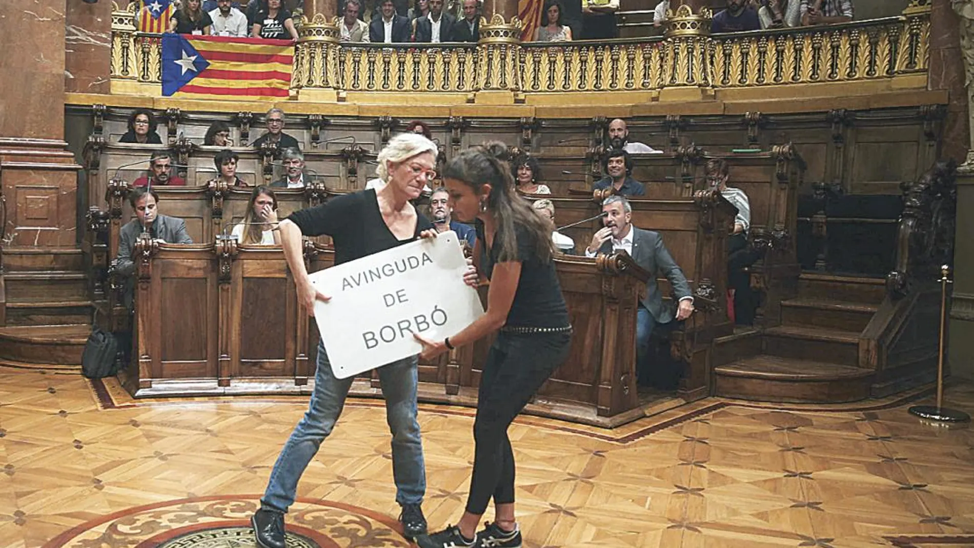 Imagen de las dos concejalas de la CUP en un pleno del Ayuntamiento de Barcelona con el cartel de la calle