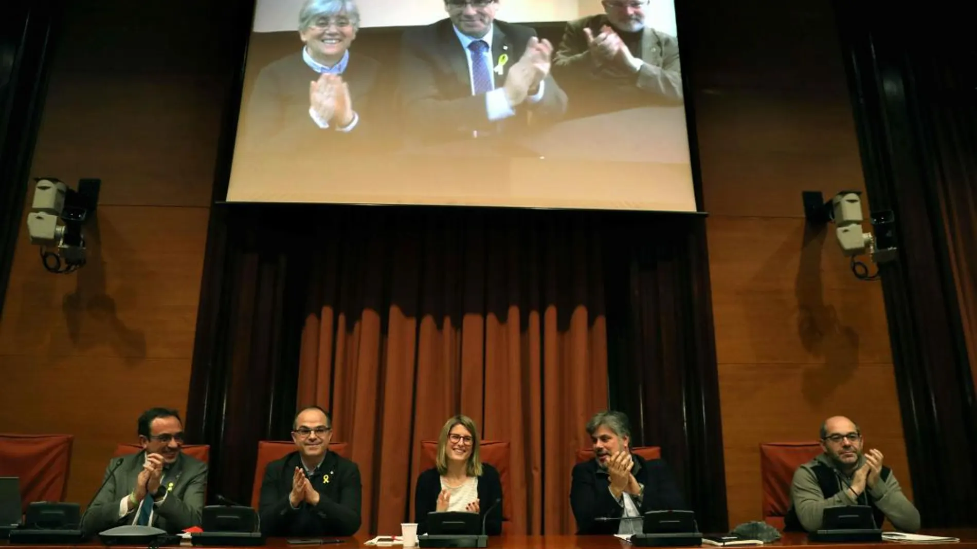 Los diputados electos Carles Puigdemont (c), Clara Pontasí (i) y Lluís Puig (d), participaron telemáticamente desde Bruselas en la reunión celebrada en el Parlament por el grupo parlamentario de Junts per Catalunya