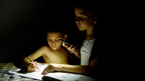 Dos niños estudian con la luz de móvil durante un apagón en Maracaibo (Venezuela)