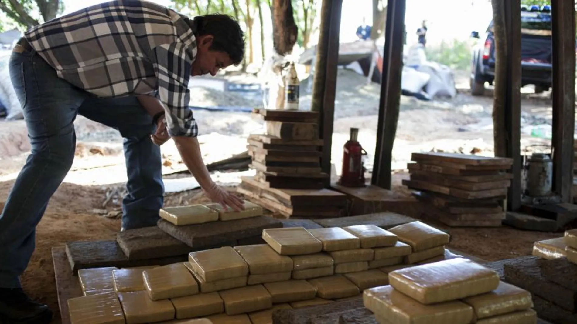 Un hombre junto a varias placas de marihuana prensada, incautada por agentes de la Secretaría Antidroga de Paraguay (Senad).