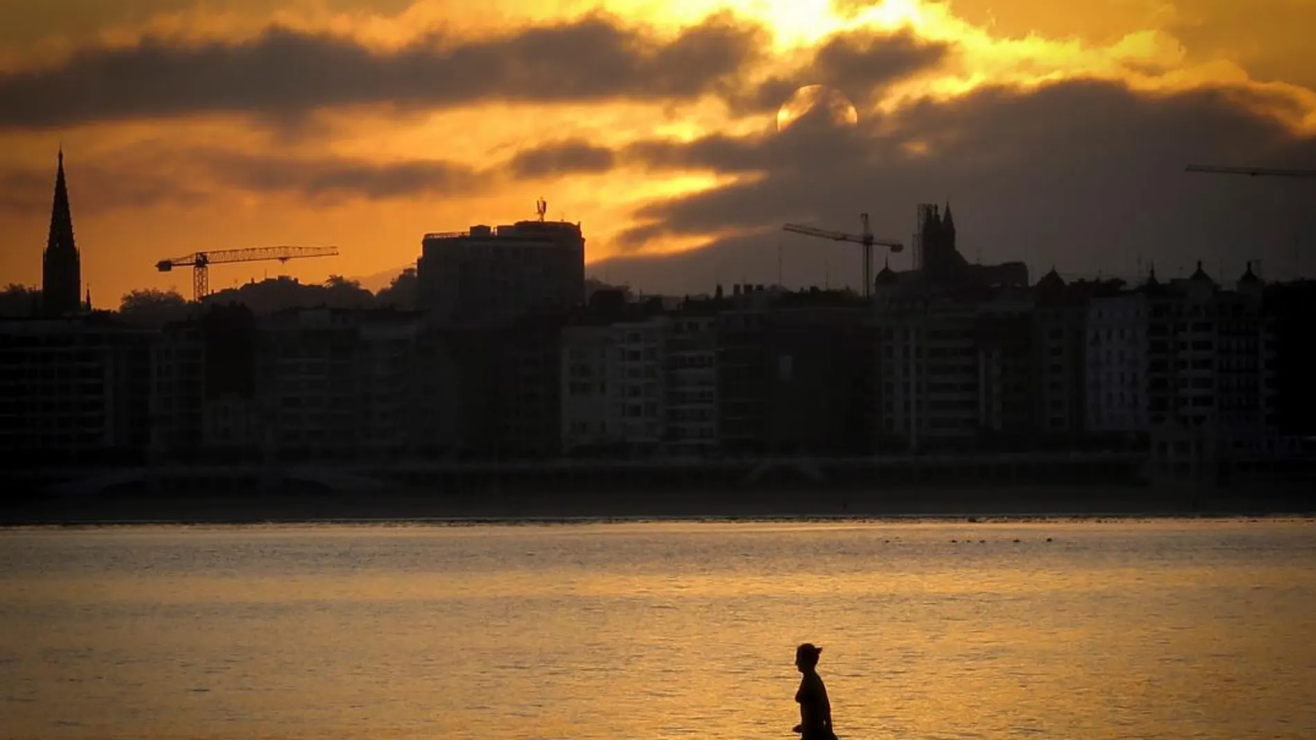 Una mujer se baña al amanecer en la playa de Ondarreta en San Sebastián / Efe