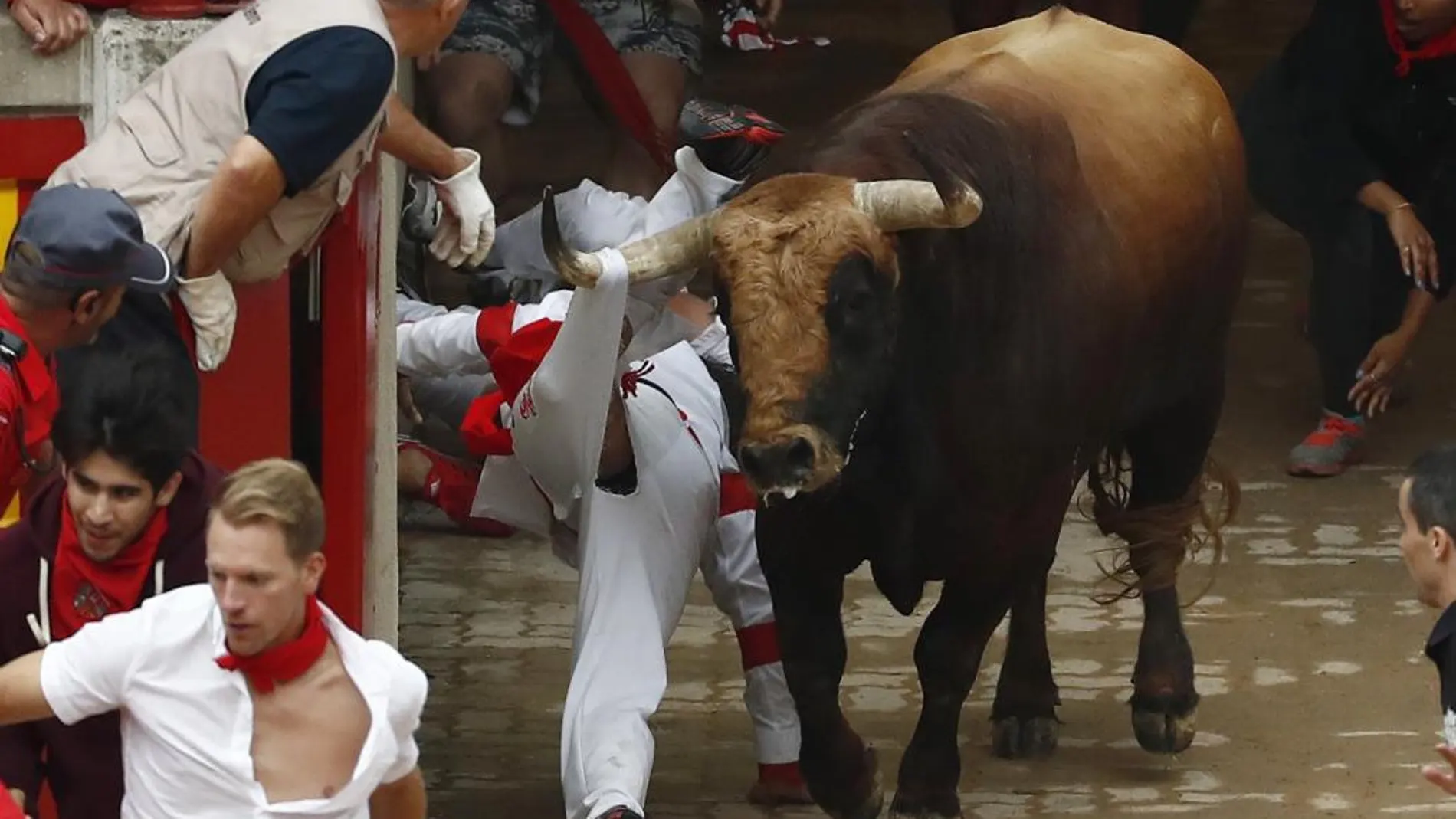 El toro "Huracán"de la debutante ganadería salmantina de Puerto de San Lorenzo engancha a un mozo en el callejón, a la entrada a la plaza de toros, durante el tercer encierro de los Sanfermines 2017