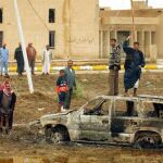 Varios iraquíes junto a uno de los vehículos quemados en los que viajaban siete agentes españoles del Centro Nacional de Inteligencia que murieron en una emboscada en 2003