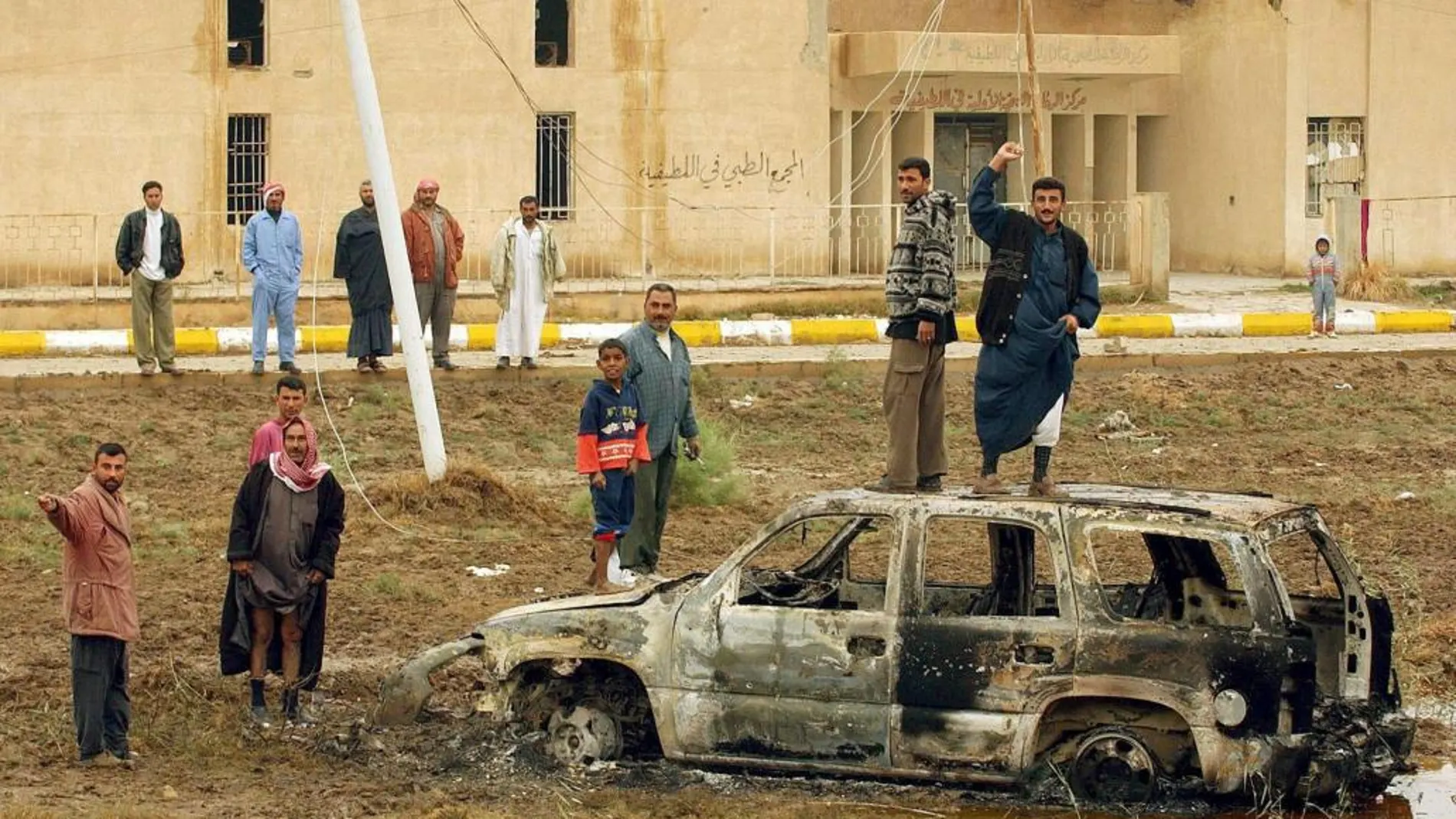 Varios iraquíes junto a uno de los vehículos quemados en los que viajaban siete agentes españoles del Centro Nacional de Inteligencia que murieron en una emboscada en 2003