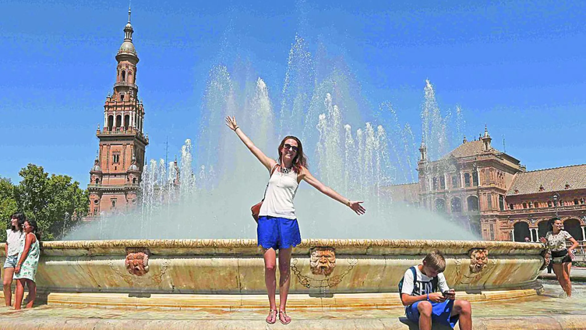 Unos turistas se refrescan en la fuente de la Plaza de España en Sevilla.