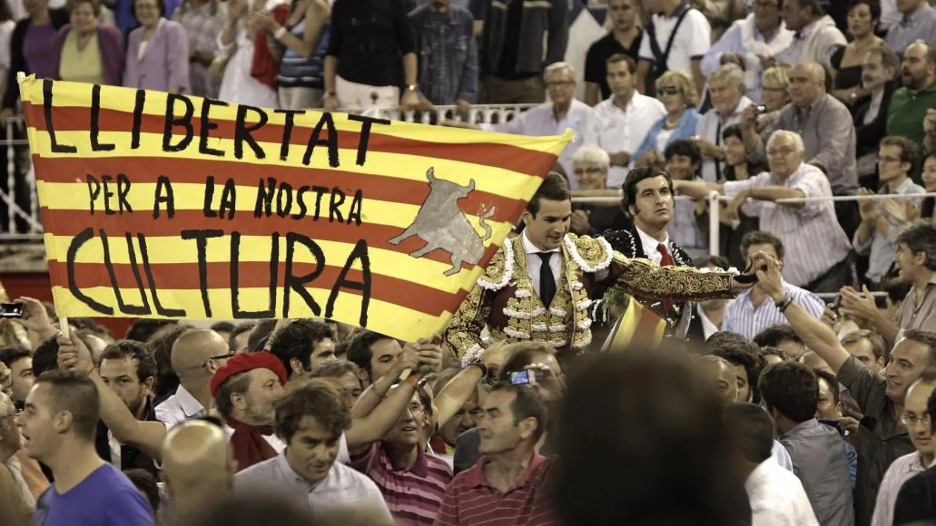 El torero José María Manzanares (2d) y "Morante de la Puebla"(d) salen a hombros por la Puerta Grande acompañados por una 'senyera' con el lema "Llibertat per a la nostra cultura"tras el penúltimo festejo taurino celebrado en la Monumental de Barcelona