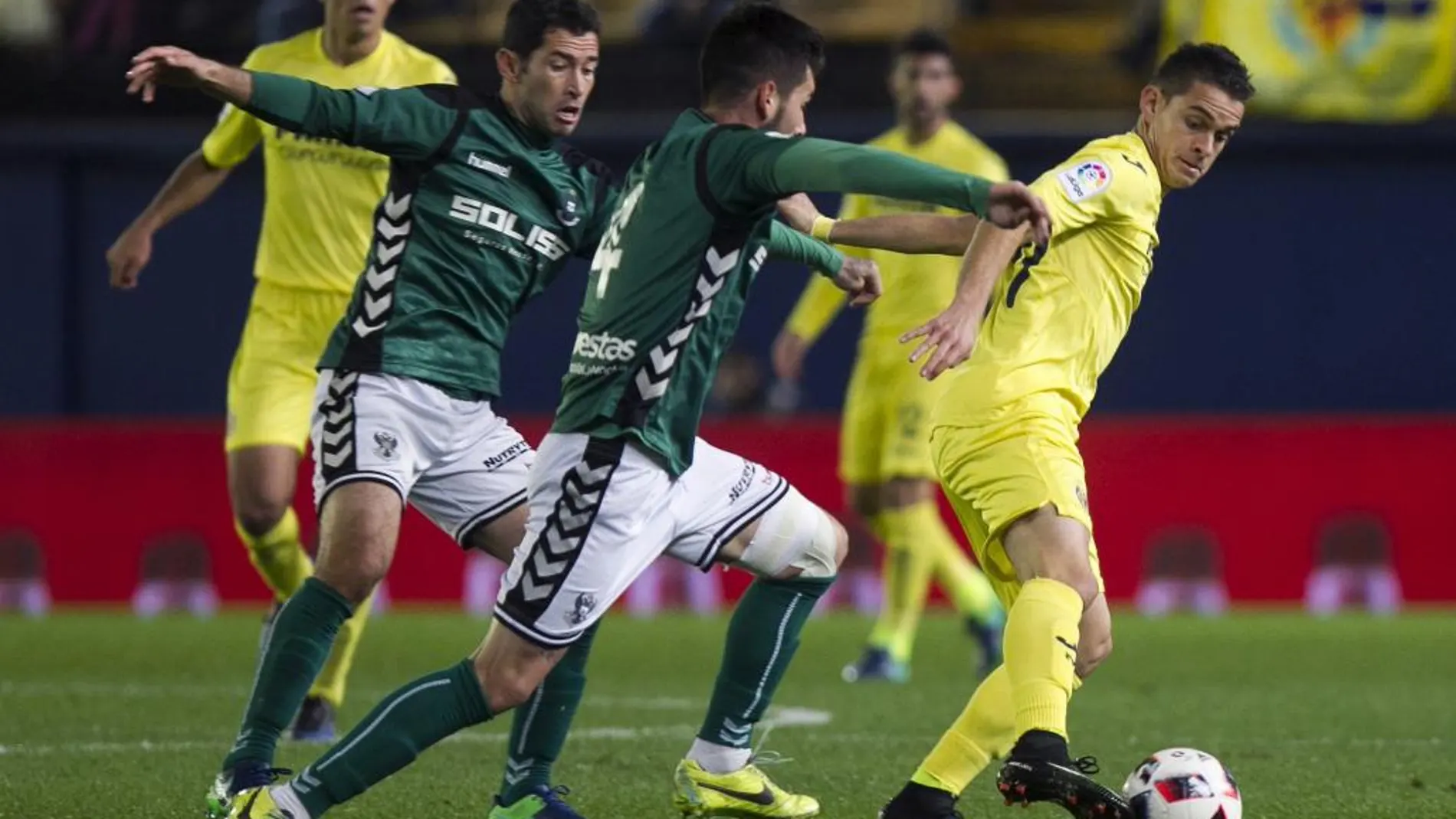 El delantero del Villarreal Santos Borre (d) pelea un balón con el defensa del CD Toledo Daniel Pérez (c) y el centrocampista Israel Castro durante el partido