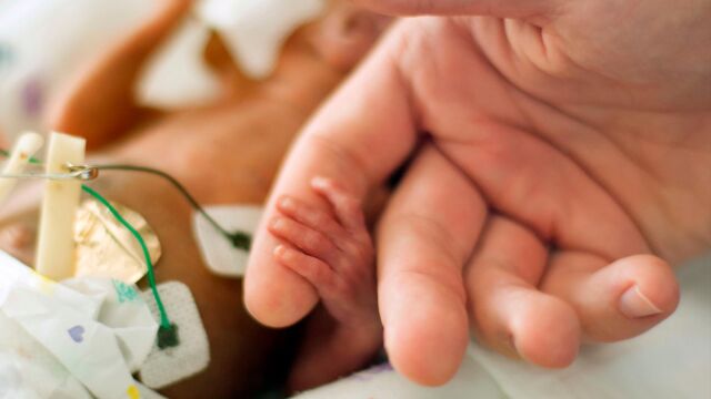 Un padre de la mano a su bebñe prematuro / Dreamstime