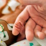 Un padre de la mano a su bebñe prematuro / Dreamstime