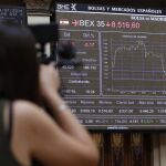 Un mujer fotografía un panel con información del principal indicador de la Bolsa española, el IBEX 35