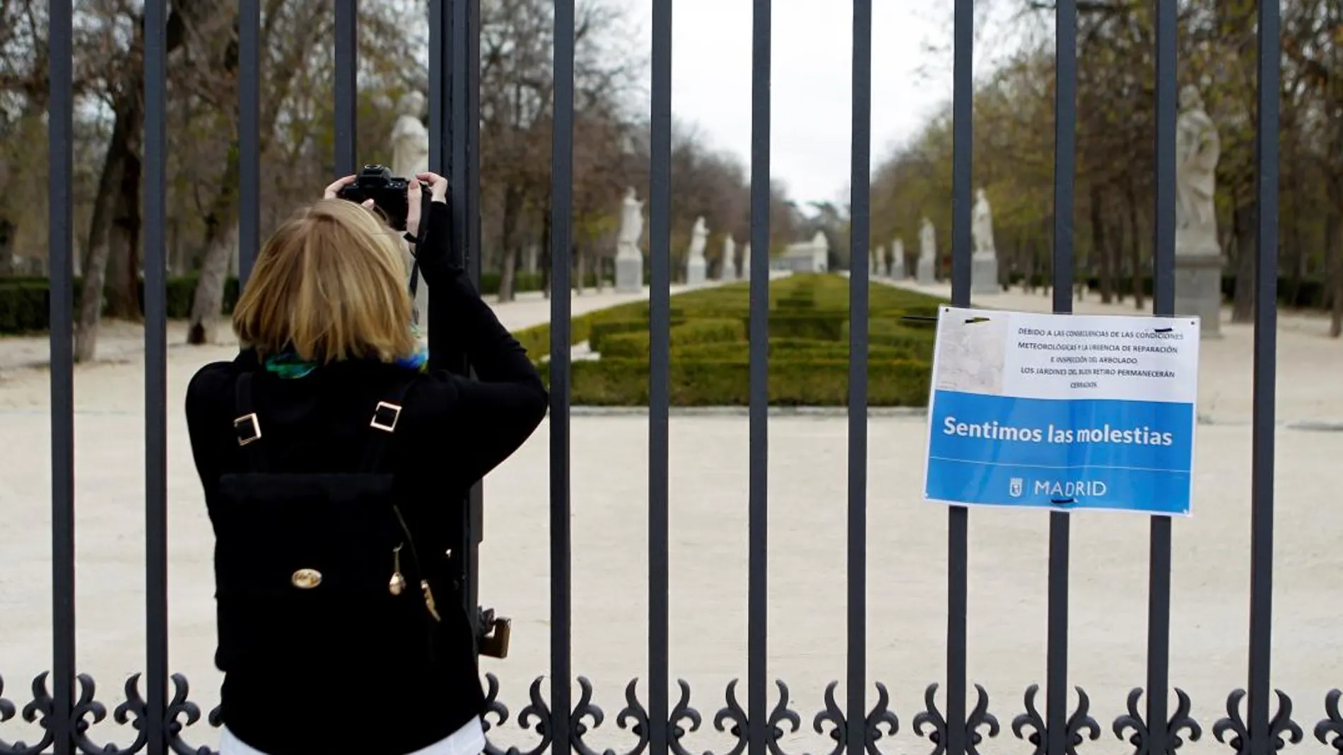 Una mujer toma una instantánea desde una de las puertas del parque del Retiro, cerrado por el Ayuntamiento de Madrid y que reabrirá hoy sus puertas