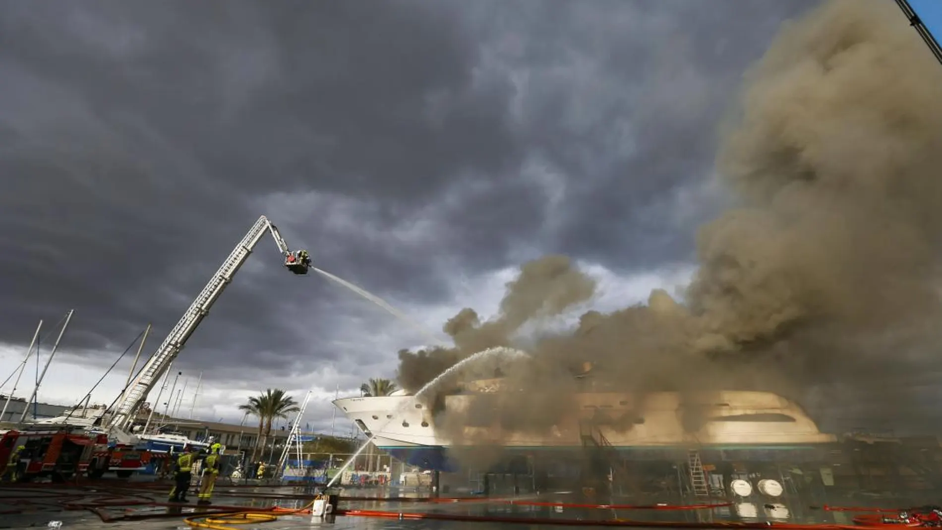 Los bomberos trabajan en la extinción del incendio del yate estacionado en un dique seco del puerto de Alicante