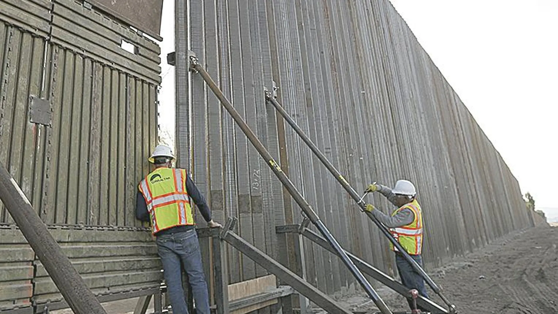 Dos empleados aseguran una sección del muro que separa México de California