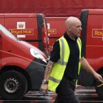 Un trabajador del servicio británico de correos Royal Mail camina junto a varias furgonetas de reparto en su sede en Londres