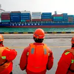 Varios trabajadores observan el paso de un barco contenedor con mercancías chinas