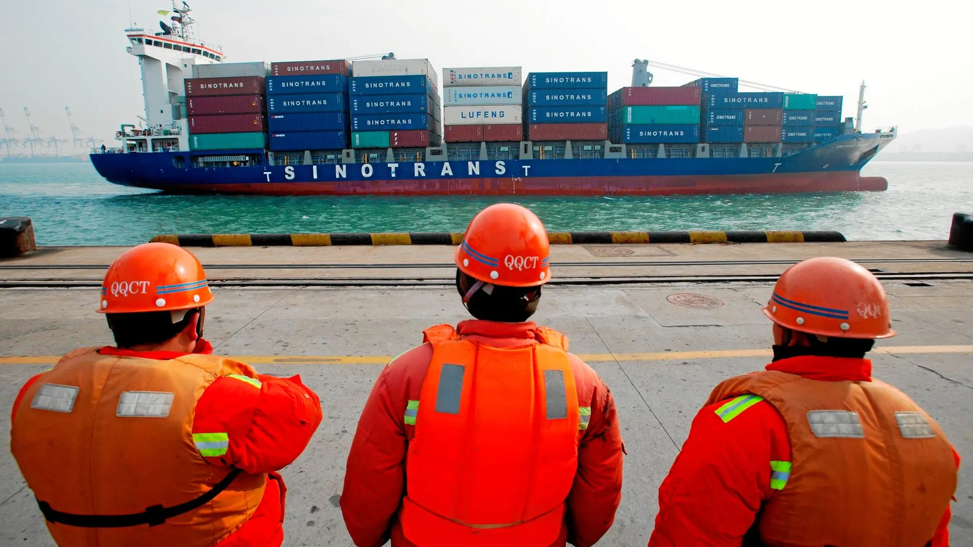 Varios trabajadores observan el paso de un barco contenedor con mercancías chinas