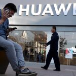 Un pequinés consulta un móvil mientras habla por otro ante una tienda del gigante chino Huawei