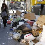 Una mujer pasa entre la basura amontonada en la calle Amaniel