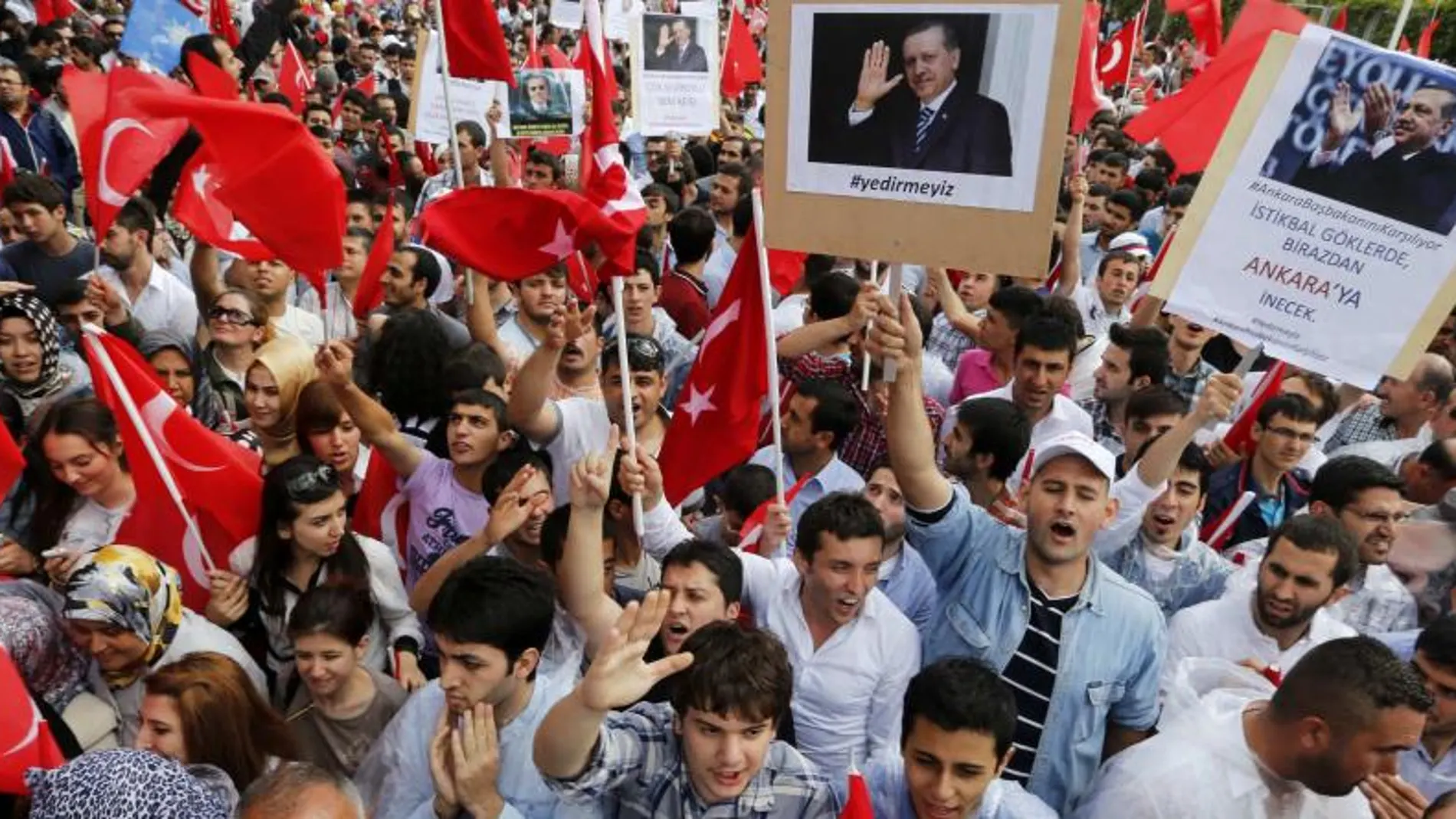 Partidarios del primer ministro Tayyip Erdogan ondean banderas de Turquía, sostienen pancartas y consignas grito mientras esperan su llegada en el aeropuerto de Esenboga en Ankara
