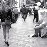 Un hombre pide limosna mientras varios ciudadanos pasean por el centro de una ciudad alemana