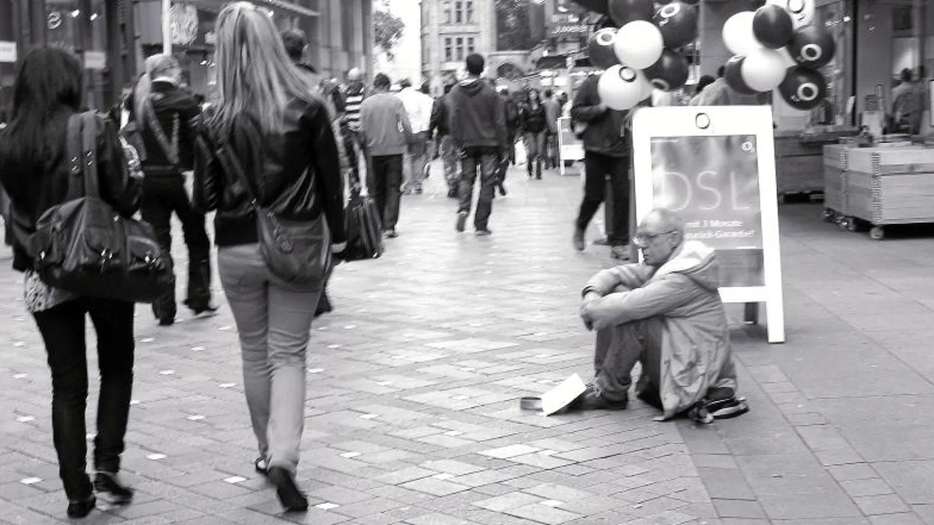 Un hombre pide limosna mientras varios ciudadanos pasean por el centro de una ciudad alemana