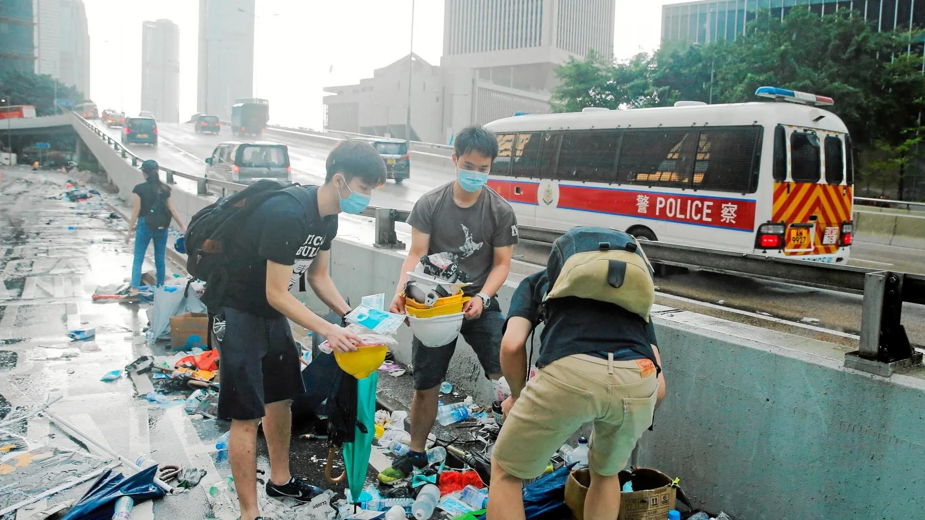 Varios jóvenes recogen cascos y paraguas de entre la basura generada tras las cargas policiales / Reuters