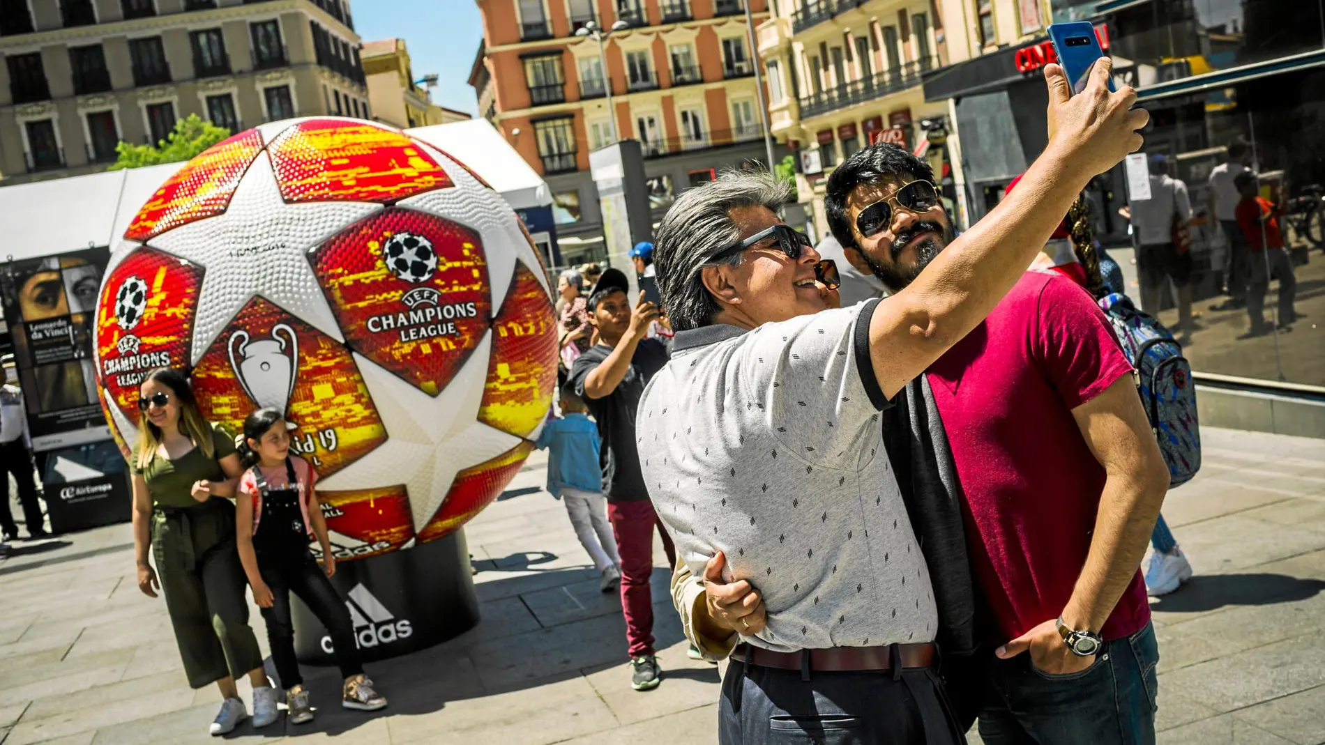 Dos aficionados posan junto a una imagen del balón de la final en la plaza de Callao. Foto: Alberto R. Roldán