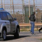 Tres inmigrantes pasean junto a la frontera de Melilla ante la atenta mirada de una patrulla de la Guardia Civil